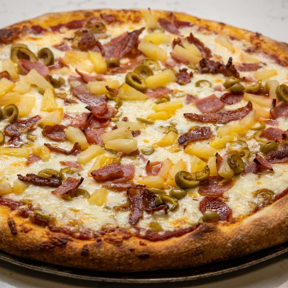 Large baked pizza topped with melted cheese, pineapple, sliced green peppers, ham, and bacon on a black serving tray.