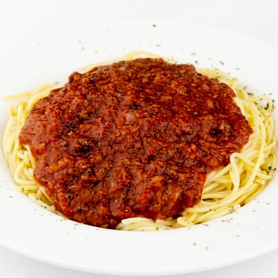 Spaghetti topped with chunky meat sauce and sprinkled herbs on a white plate.